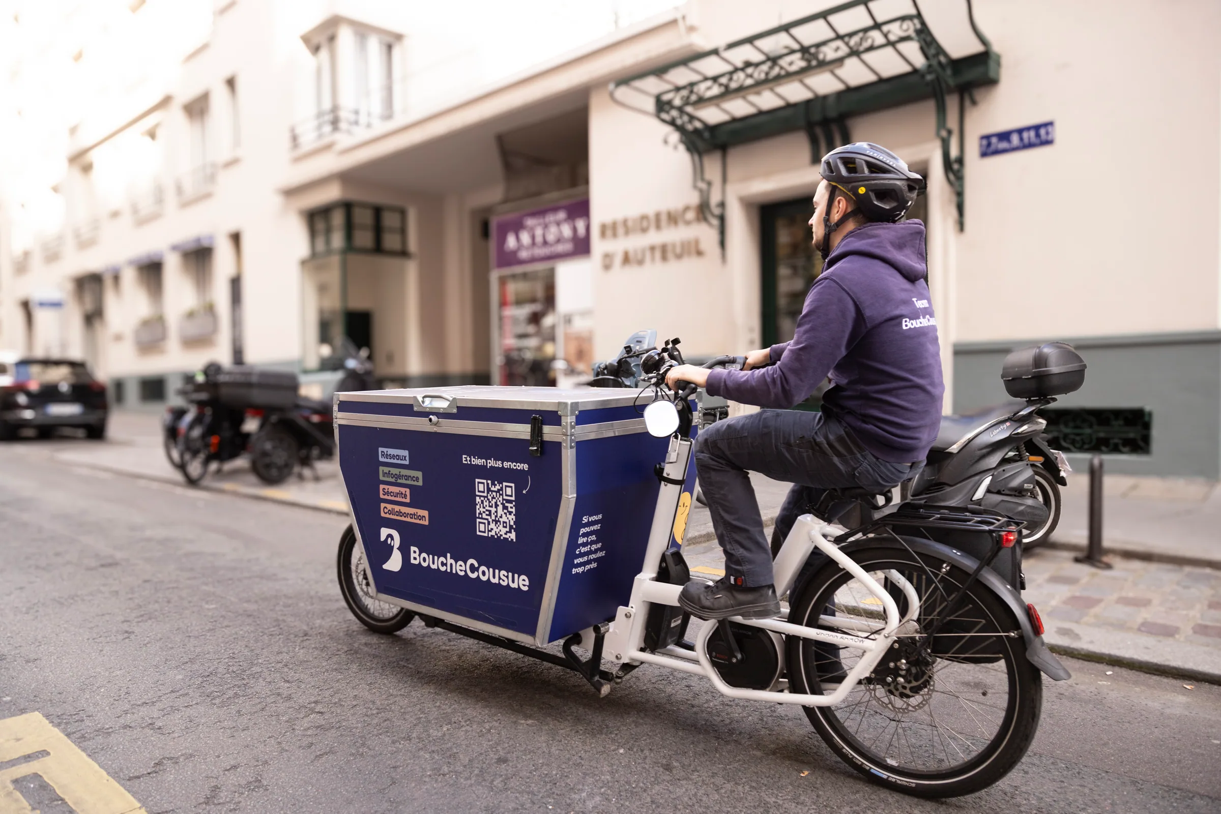 Technicien BoucheCousue circulant à vélo cargo dans une rue parisienne